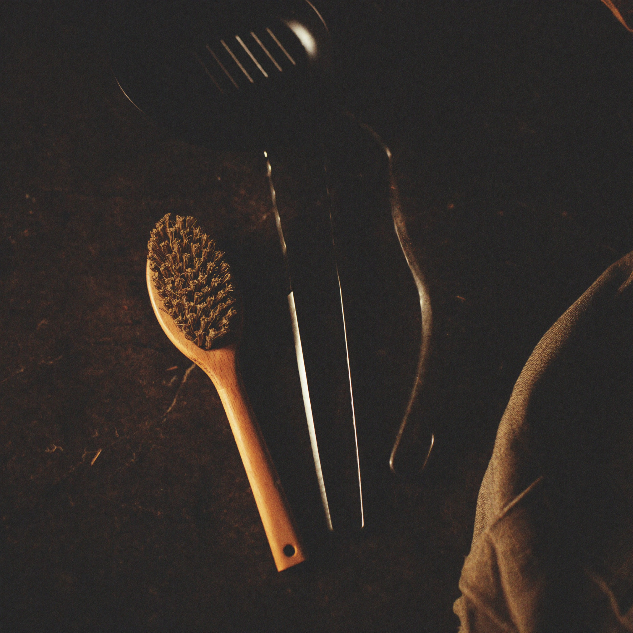 Editorial-Stillleben mit geschwärzten Grillzangen, Bürste, Gusseisenpfanne und Leinentuch auf Stein